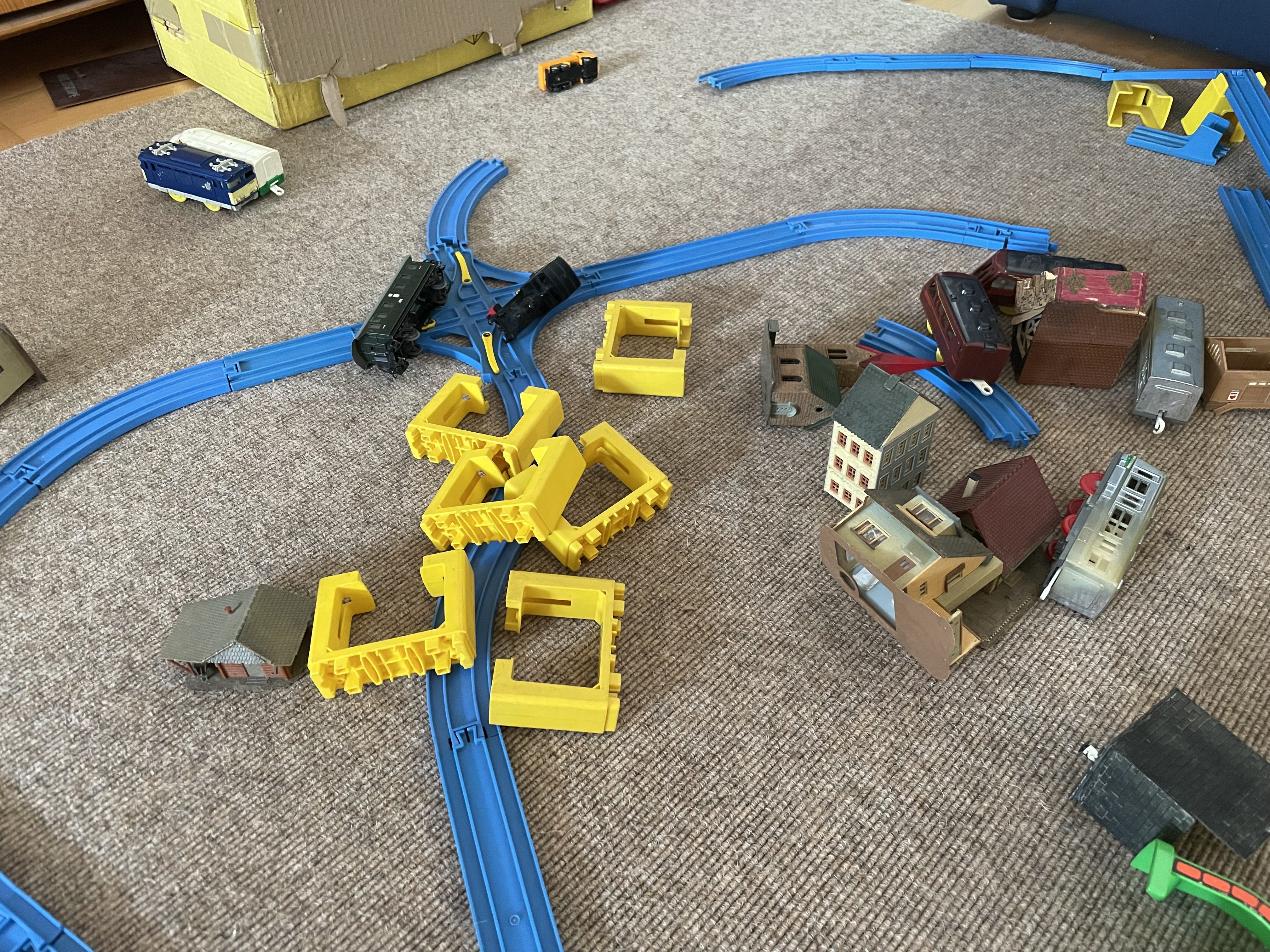 Spielzeugeisenbahn auf einem Teppich, diverse Wagen, Brückenteile und Häuser sind umgekippt und liegen wild verstreut in der Gegend herum